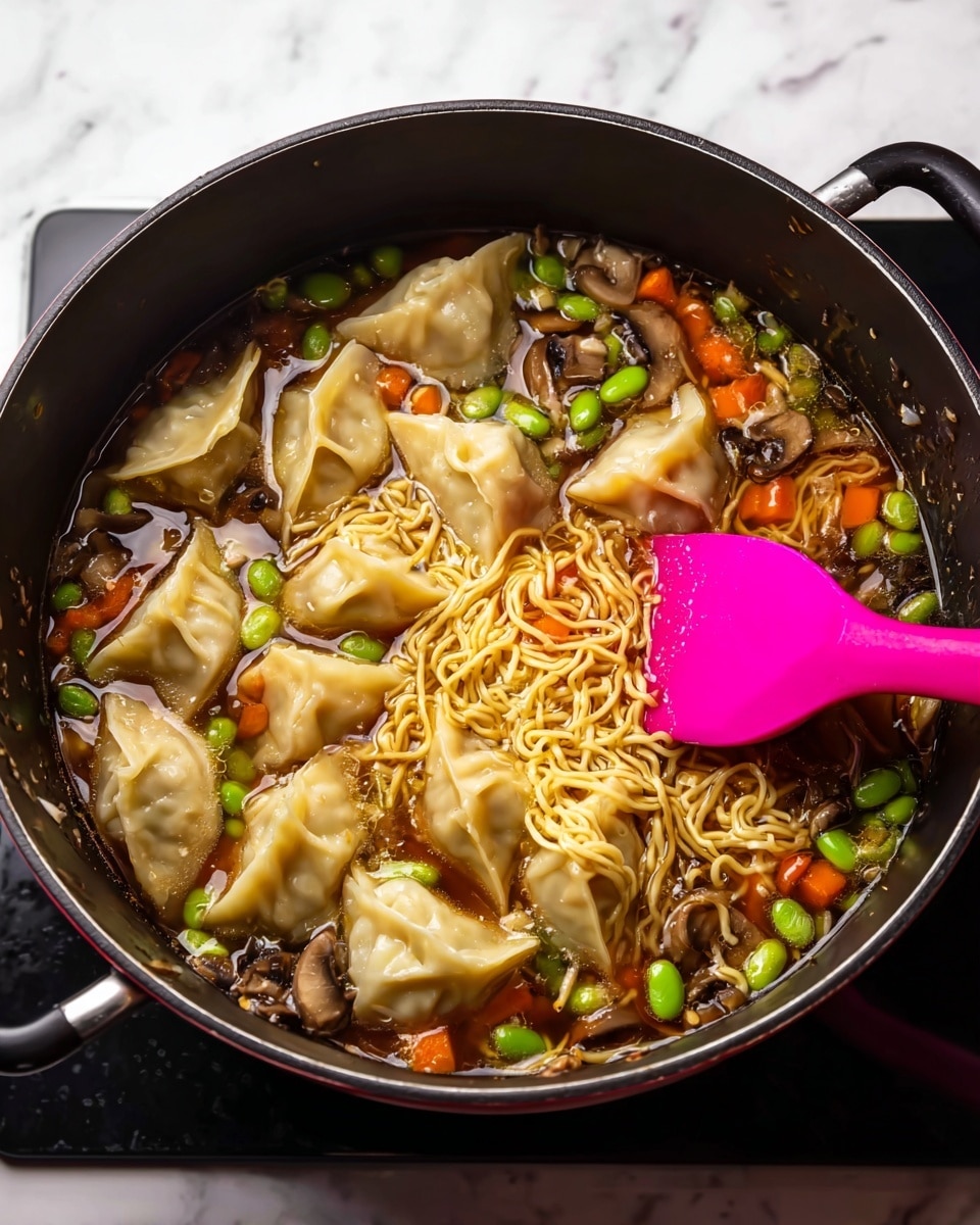 A black pot filled with light brown broth holds thin yellow noodles spread through the middle and bottom. On top of the noodles are light beige dumplings with slightly wrinkled edges arranged in a loose circle. Bright green edamame beans and small orange carrot cubes float around the noodles along with sliced brown mushrooms. A bright pink spatula rests on the right side, partly in the broth, stirring the noodles. The pot handles are visible on the sides, all set on a white marbled surface photo taken with an iphone --ar 4:5 --v 7