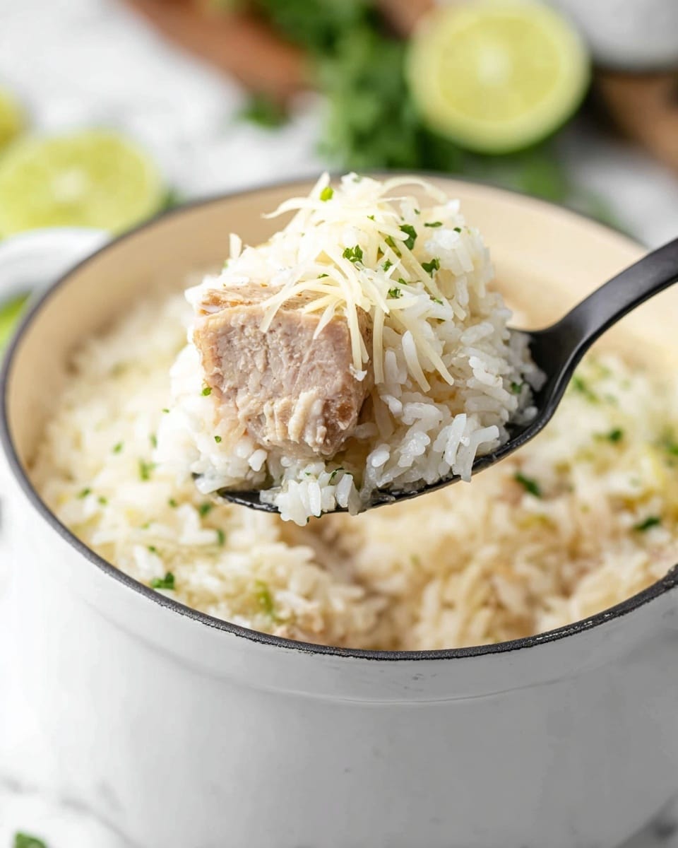 A white pot filled with soft, white rice mixed with small green herbs sits on a white marbled surface. A black spoon lifts a scoop showing three layers: the bottom layer is cooked white rice with a fluffy texture, the middle layer is a piece of tender light brown meat, and the top layer is finely shredded white cheese mixed with tiny green herb bits. In the background, blurred lime slices and green herbs add color contrasts. The scene is bright and clean. photo taken with an iphone --ar 4:5 --v 7