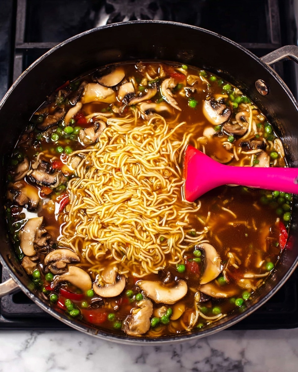 A large black pot is filled with dark brown broth, thin yellow noodles floating in the center, surrounded by many sliced white and brown mushrooms, bright green peas, and red bell pepper pieces. A pink silicone spatula is stirring the soup from the right side, creating ripples in the broth, and the pot is placed on a stove with a white marbled surface beneath it. The ingredients are mixed but clearly seen individually, showing a colorful, fresh noodle soup. photo taken with an iphone --ar 4:5 --v 7