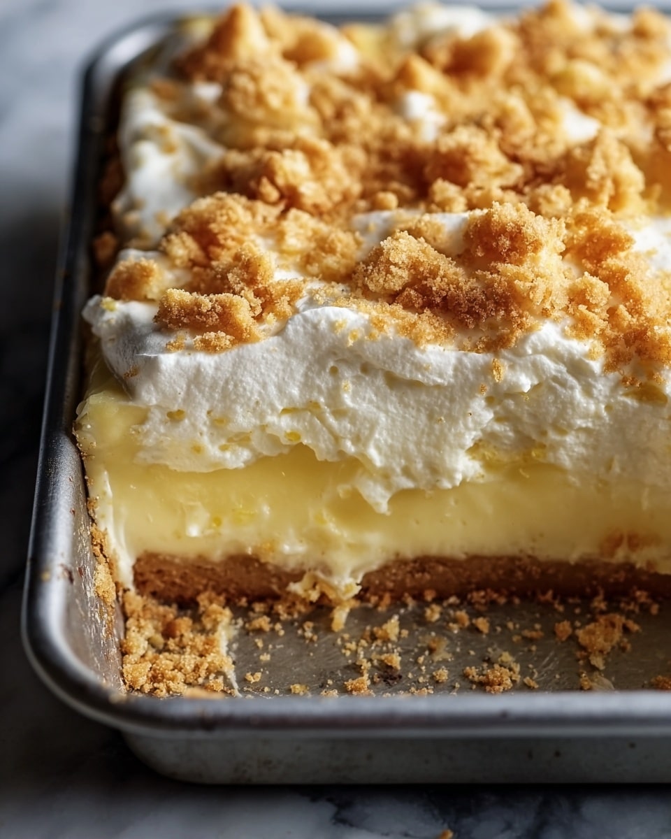 A close-up image of a three-layer lemon dessert in a metal baking pan on a white marbled surface. The bottom layer is a light brown, crumbly crust with some crumbs scattered around. Above that is a thick, smooth, pale yellow lemon filling. The top layer consists of white, fluffy whipped cream mixed with golden brown, crunchy crumbs sprinkled unevenly across the surface. The edges of the pan show slight browning and a rustic feel. Photo taken with an iphone --ar 4:5 --v 7