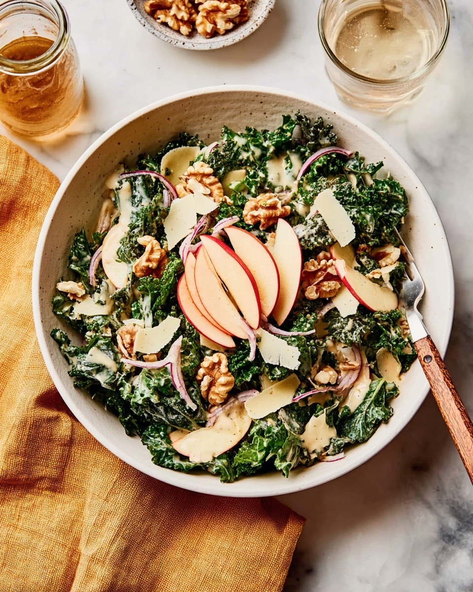 A white bowl filled with a fresh kale salad as the base layer, dark green and slightly wrinkled. On top, thin slices of red apple arranged in a semi-circle, adding a light red and cream color. Scattered across are chunks of light brown walnuts. Thin, pale shavings of cheese are spread unevenly over the salad. There are a few small pieces of red onion mixed in among the layers. The salad is dressed with a creamy, beige sauce drizzled lightly over everything. To the right side of the bowl, a fork with a wooden handle rests on the edge. The bowl is placed on a white marbled surface next to a folded mustard-yellow cloth napkin, a partially visible clear glass of water, and a small jar with sauce. Photo taken with an iphone --ar 4:5 --v 7