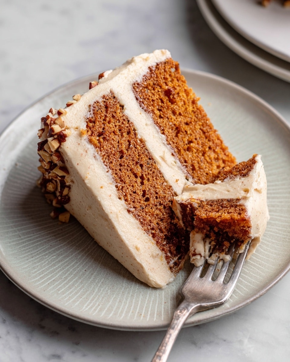 A slice of two-layer brown cake with a soft texture sits on a white plate, showing two thick layers of light brown cream frosting between the cake layers and covering the top and sides. Small chopped nut pieces are sprinkled on the top edge of the frosting. A silver fork rests on the plate, holding a piece of the cake with frosting. The plate is placed on a white marbled surface. Photo taken with an iphone --ar 4:5 --v 7