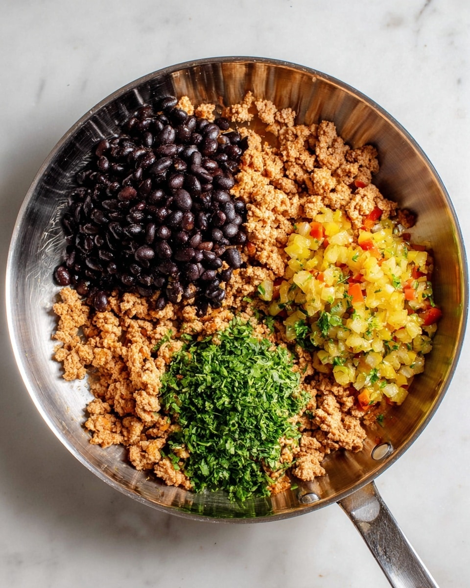 A metal pan holds four main layers: cooked ground meat spread evenly forming the base with a light brown and crumbly texture, black beans piled in a shiny dark cluster on the left side, diced yellow-green vegetable mixture with small red bits on the bottom right, and finely chopped fresh green herbs scattered near the center and right side. The shiny pan contrasts with the white marbled surface below. photo taken with an iphone --ar 4:5 --v 7