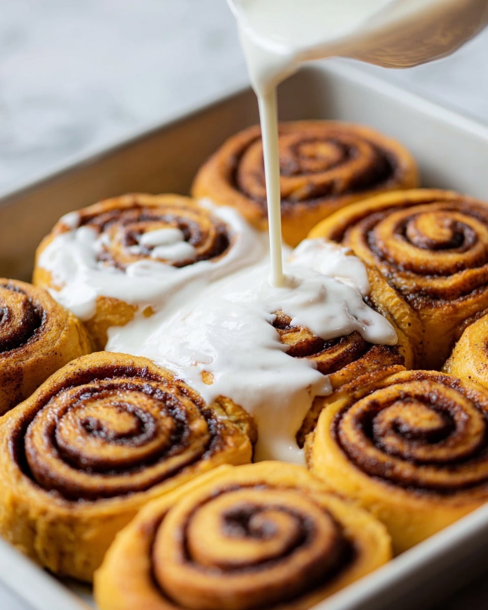 A close-up view of nine golden-brown cinnamon rolls placed closely in a white tray, each roll showing clear dark brown cinnamon spirals on top. A woman's hand is pouring thick white cream over the center cinnamon roll, with some cream spreading unevenly over the adjacent rolls. The rolls have a soft, slightly rough texture, and the contrast between the white cream and the cinnamon spirals highlights the swirl pattern. The tray sits on a white marbled surface, adding a clean, bright look to the scene. photo taken with an iphone --ar 4:5 --v 7