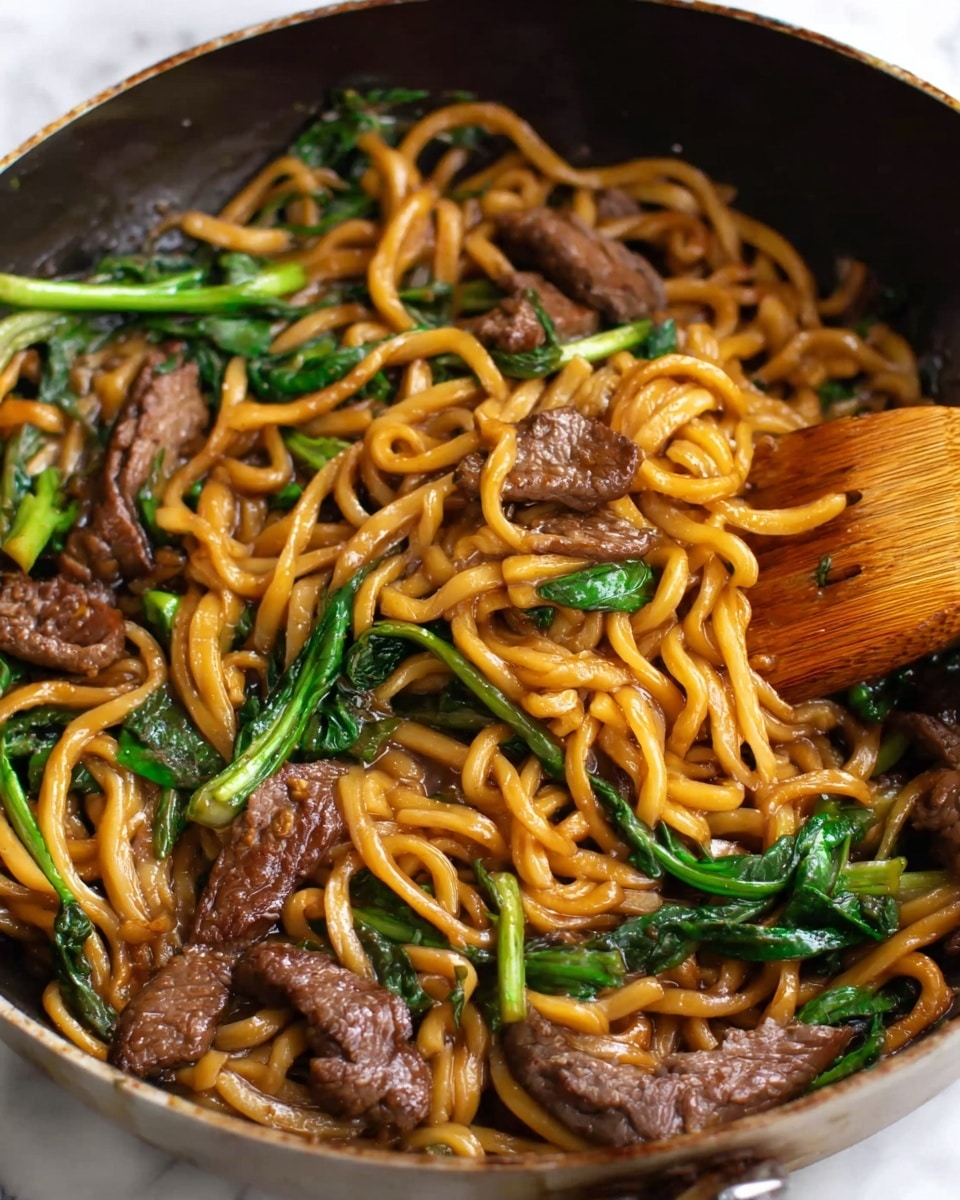 The image shows a close-up of a cooked noodle dish inside a pan. The dish has thick yellowish-brown noodles that are twisted and layered all over. Mixed in are several pieces of dark brown cooked meat with a soft, slightly wrinkled texture, spread evenly across the dish. Green leafy vegetables with fresh bright green stems and leaves are scattered throughout, adding color contrast. A wooden spatula is partially visible on the right side, lifting some noodles and meat. The background is a white marbled texture. Photo taken with an iphone --ar 4:5 --v 7