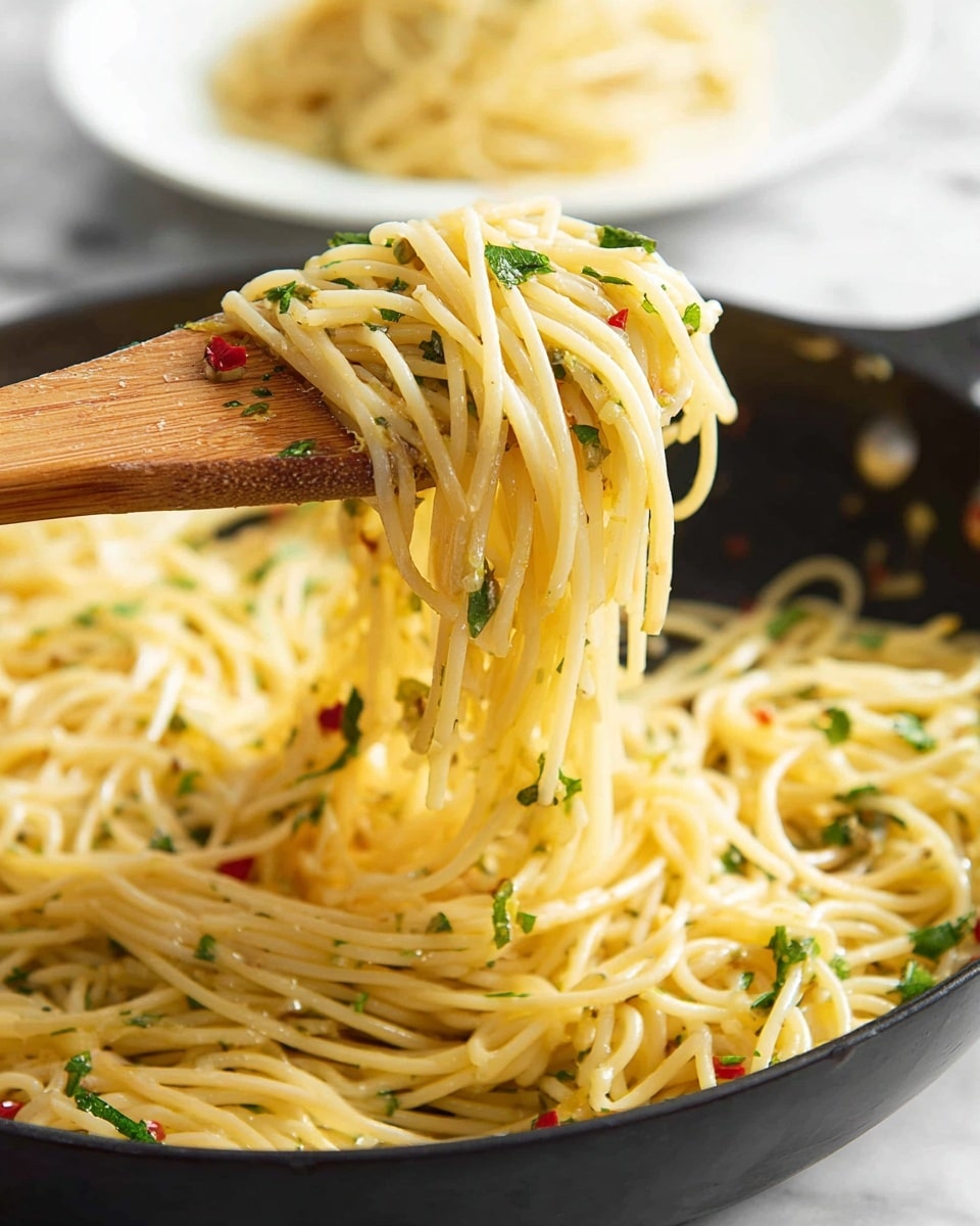 A close-up view shows a pile of spaghetti pasta cooked and mixed with small green herb pieces and tiny red chili flakes, giving texture and color. The pasta strands are lifted by a wooden spoon, showing the noodles hanging in mid-air with a slightly shiny, smooth surface. The pasta rests in a black pan filled nearly to the top with more strands, and in the blurred background, there is a white plate with more cooked spaghetti. The scene is set on a white marbled surface. photo taken with an iphone --ar 4:5 --v 7