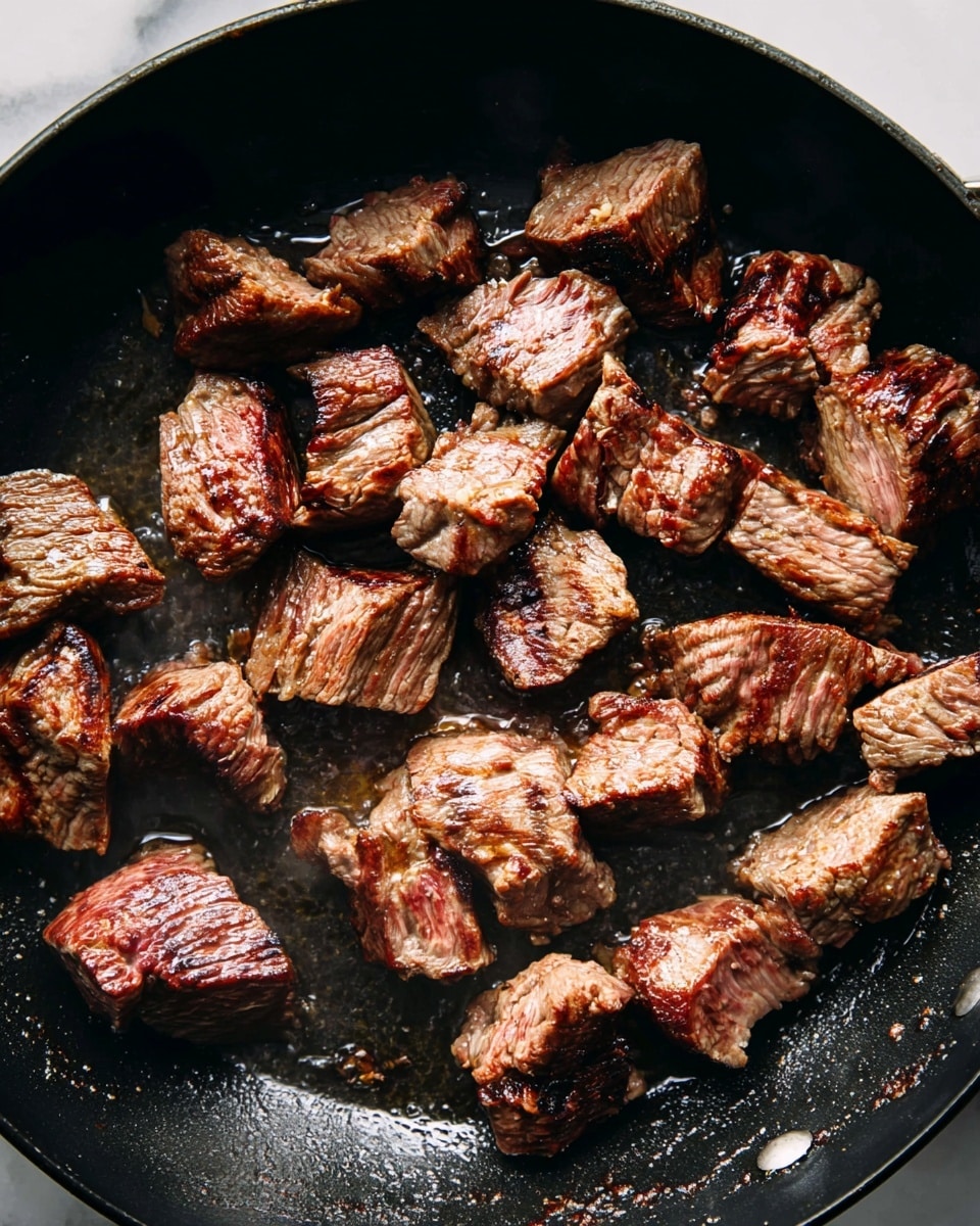 The image shows multiple pieces of browned meat sautéing in a black pan, each piece uneven in size with a textured surface showing grill marks and slight charring. The meat has a mix of deep brown and pinkish hues, indicating some parts are still cooking, while the pan surface is glossy with cooking juices and oil. There is no garnish or additional ingredients visible. The setting features a white marbled texture visible around the pan edges. photo taken with an iphone --ar 4:5 --v 7