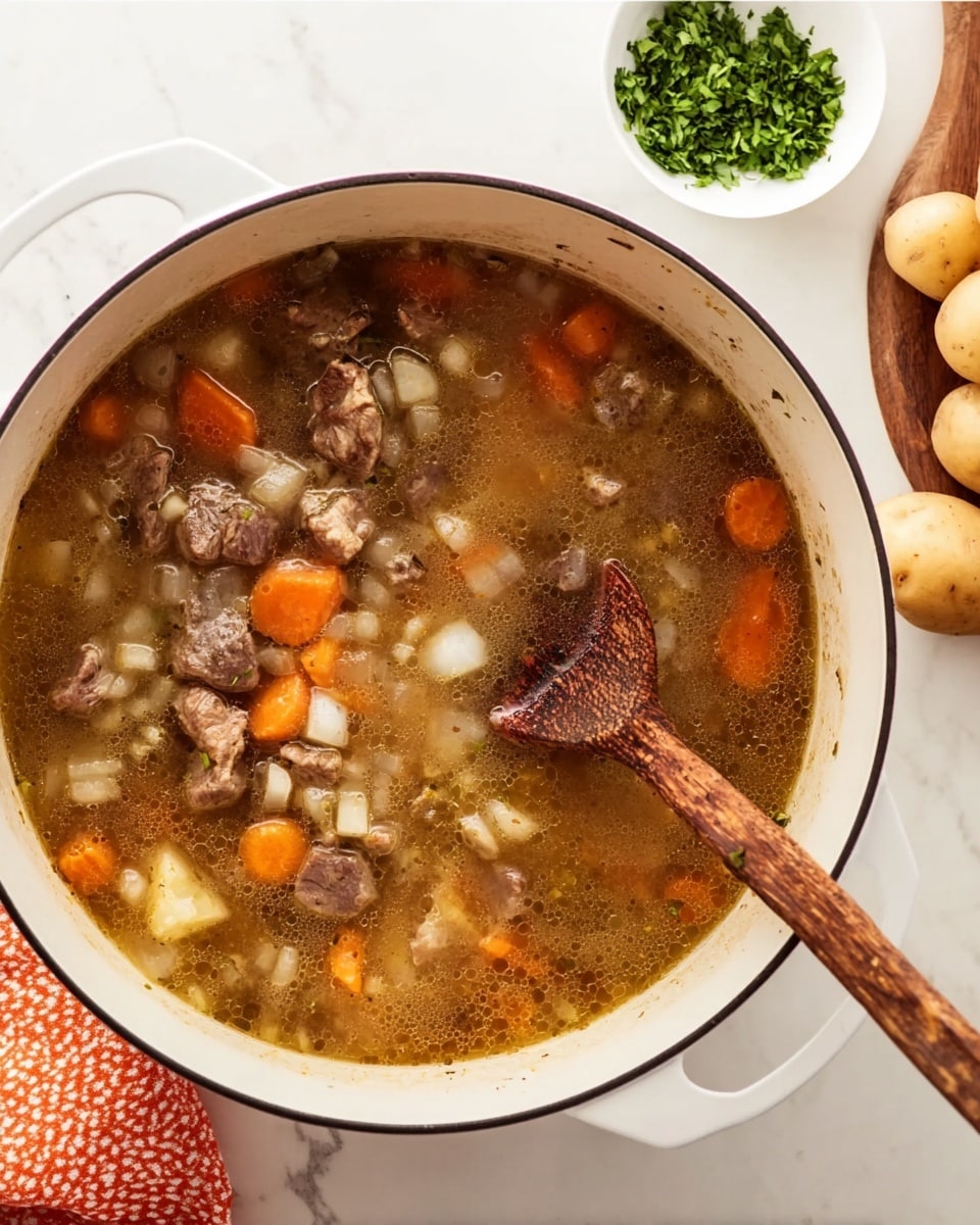 A white pot filled with a warm stew showing about three layers: at the bottom, a light brown broth; the middle layer contains chunky pieces of brown meat and translucent diced onions; the top layer has small orange carrot slices floating. A wooden spoon with a grainy texture rests inside the pot on the right side, partly submerged in the stew. The pot sits on a white marbled surface with some whole potatoes visible in the top right corner and a small white bowl of chopped green herbs in the top left corner. An orange and white patterned cloth is partially visible on the bottom left side photo taken with an iphone --ar 4:5 --v 7