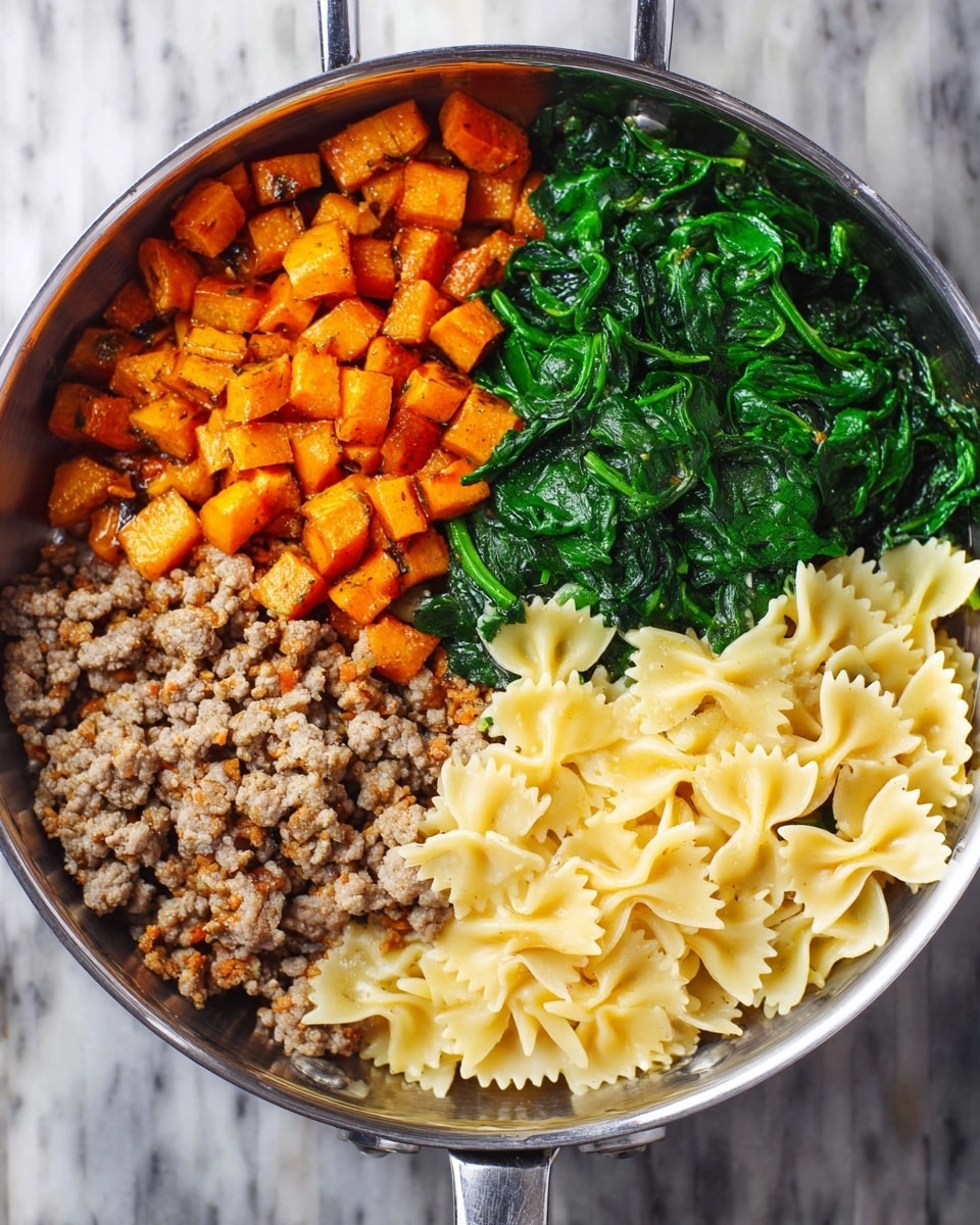 A stainless steel pan shows four sections of food. One section has small orange roasted cubes with a slightly crispy texture. Next to it is a bright green layer of cooked spinach with a soft, wilted look. Below the spinach is a cooked ground meat layer with a lightly browned, crumbly texture. The last section contains light yellow bowtie pasta, dry and separated, filling its quarter of the pan. The pan sits on a white marbled surface. photo taken with an iphone --ar 4:5 --v 7