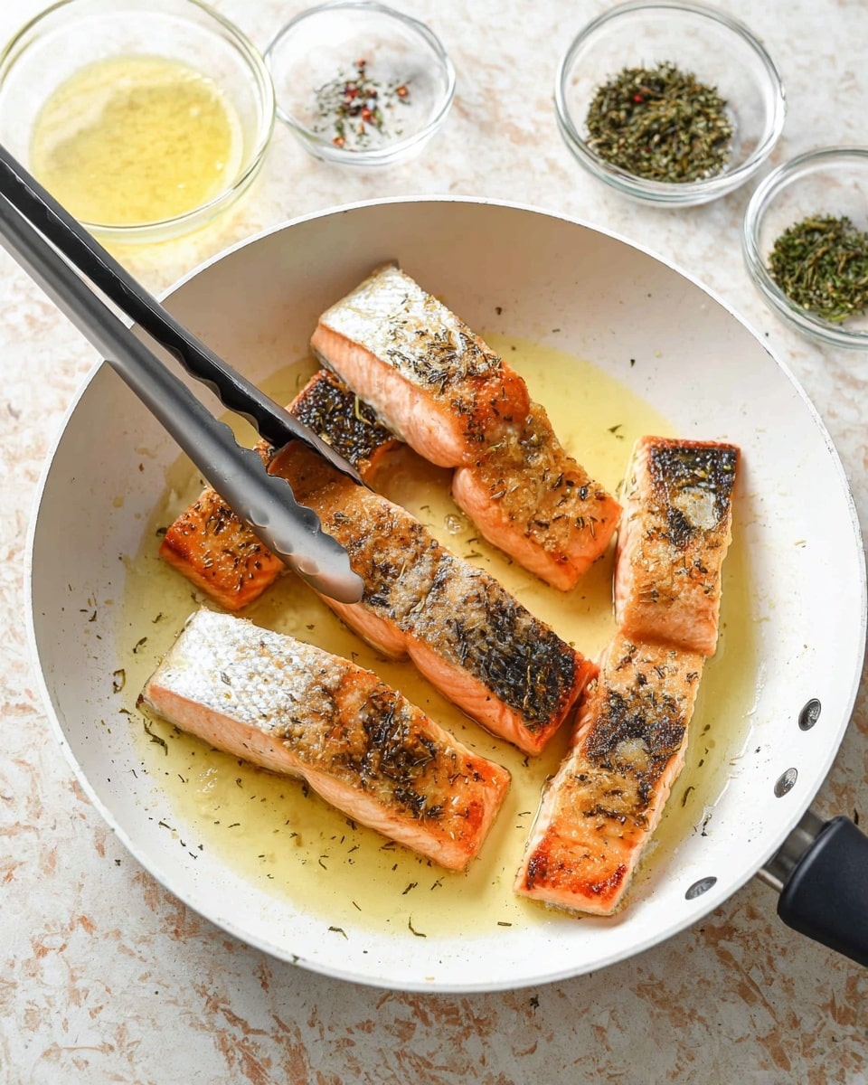 A white pan with six pieces of salmon fillets arranged inside, skin side up, showing golden brown crispy skin with some white flaky parts. The salmon pieces lie in a pool of light yellow cooking oil. Black-tipped silver tongs are holding one piece of salmon on the left side. In the background, there are three small glass bowls containing dried green herbs and a light yellow sauce on a white marbled surface. Photo taken with an iphone --ar 4:5 --v 7