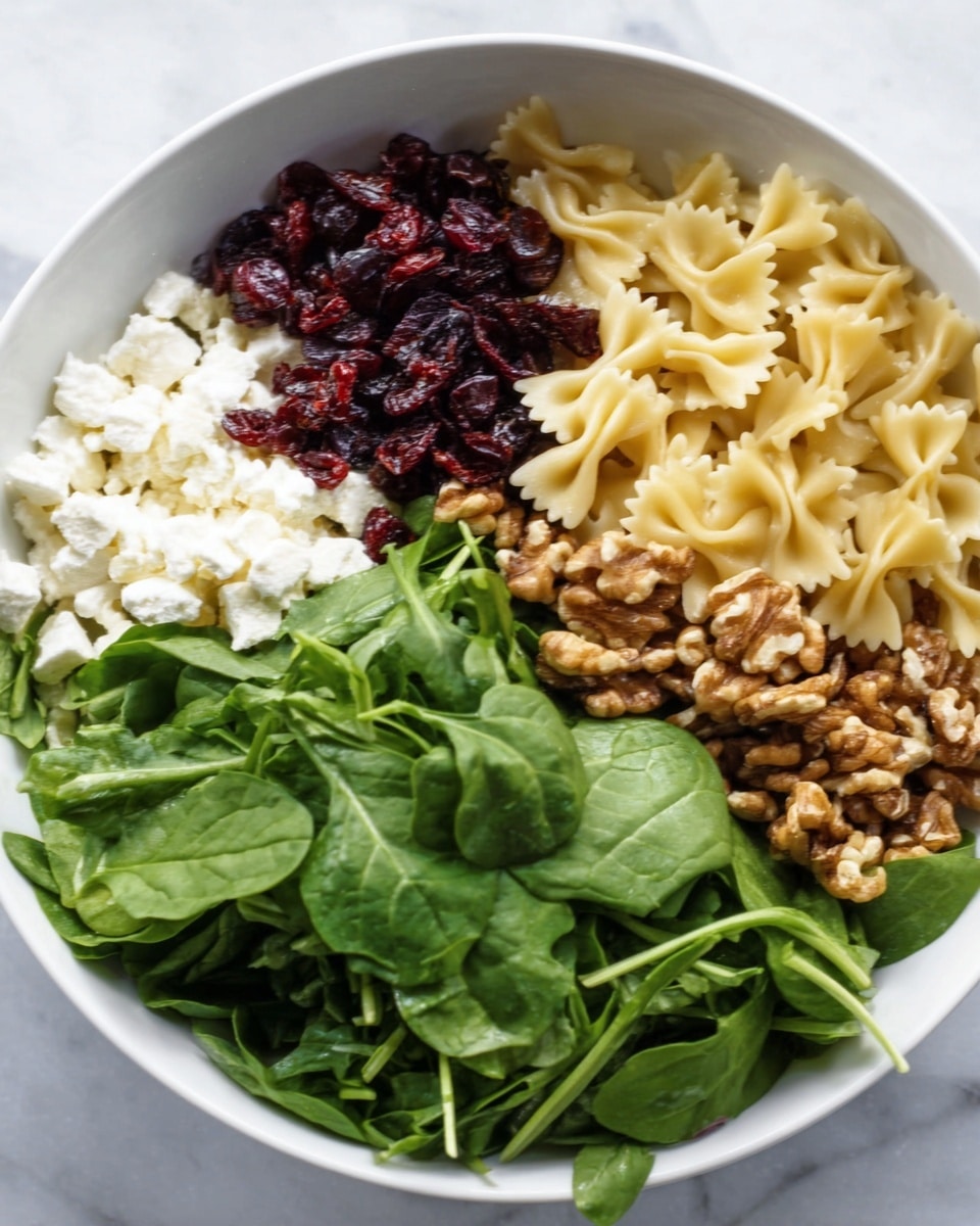 A white bowl sits on a white marbled surface filled with six distinct sections of ingredients: on the left are crumbly white cheese pieces, next to them are deep red dried cranberries, followed by light yellow bowtie pasta at the bottom right, bright green fresh spinach leaves on the top right, a pile of brown walnut halves near the center, and fresh dark green arugula leaves on the top left, all arranged side by side without mixing. photo taken with an iphone --ar 4:5 --v 7