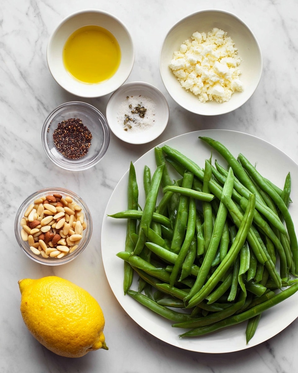 A white plate piled high with fresh, whole green beans takes up the upper right side of the frame, showing their smooth, long, slender shapes and deep green color. To the left, six small white bowls and containers hold various ingredients neatly arranged on a white marbled surface. At the top left, a bowl of light tan breadcrumbs sits beside another bowl filled with chopped brown nuts. Below these, a bowl of golden olive oil reflects light softly. Nearby, a whole bright yellow lemon adds a pop of color. At the bottom right, three small white containers hold white crumbled cheese, golden toasted pine nuts, and a mix of salt and pepper, neatly placed in a line. The overall mood is clean and fresh with a well-organized layout. Photo taken with an iphone --ar 4:5 --v 7