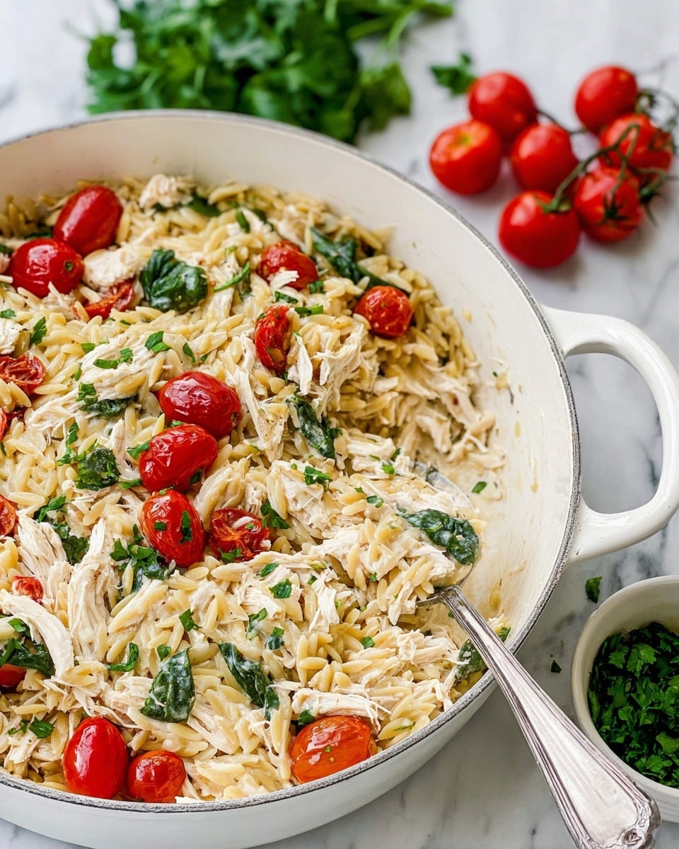 The dish is a pasta casserole served in a white deep pan with handles, placed on a white marbled surface. The casserole has several visible layers, starting with a base of creamy, light beige orzo pasta mixed with shredded white chicken pieces. Scattered throughout the orzo are bright red, whole roasted cherry tomatoes that add vibrant pops of color. Green fresh spinach leaves and roughly chopped parsley are mixed evenly on top and within the pasta, adding a fresh green contrast. The texture looks creamy and slightly thick, with a silver spoon scooping some of the mixture from one side of the pan. A few additional parsley sprigs and cherry tomatoes in the background complete the fresh presentation. Photo taken with an iphone --ar 4:5 --v 7