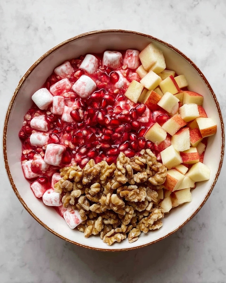 A white bowl with a brown rim sits on a white marbled surface, filled with a mix of ingredients divided into four visible sections. The first layer shows bright red pomegranate seeds scattered over small white marshmallows covered in a light red syrup. The second layer contains small, neat cubes of pale yellow apple with red skin around the edges. The third layer is a mound of chopped walnuts, light to medium brown with a rough texture. The layers are all placed side by side, filling the bowl evenly. Photo taken with an iphone --ar 4:5 --v 7