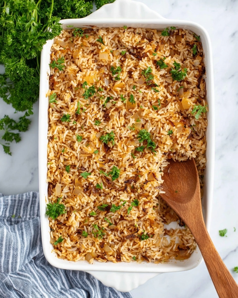 The image shows a white rectangular baking dish filled with a single layer of cooked rice that is golden brown with some darker caramelized edges, mixed with small pieces of translucent cooked onions and garnished with small green parsley leaves scattered on top. A wooden spoon is partially digging into the rice near the bottom right corner of the dish, showing the texture of the grains, which look fluffy and separated. The dish is placed on a white marbled surface with a bunch of fresh parsley on the upper left and a blue and white striped cloth partially visible on the lower left side. photo taken with an iphone --ar 4:5 --v 7