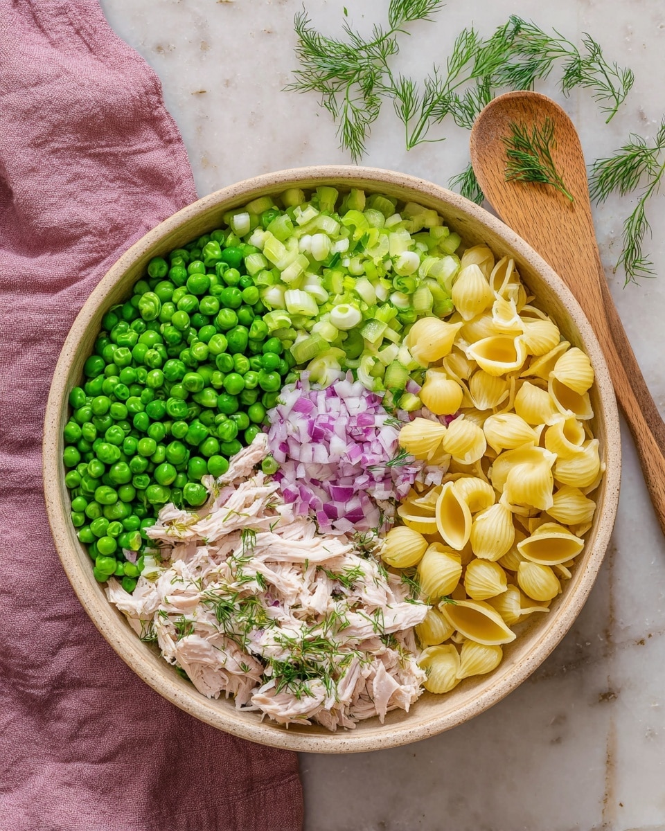 A round beige bowl on a white marbled surface holds six sections of ingredients neatly arranged. Starting from the bottom left, there is a large pile of bright green peas, next to it chopped celery in light green color. In the middle, there is a small mound of finely chopped red onions with purple and white shades. To the right of the onions, there are yellow pasta shells with a smooth texture. At the bottom right, there is shredded pale beige chicken topped with a small sprinkle of green dill. A few sprigs of dill are scattered above the onions and chicken. A pink cloth and wooden spoon lie next to the bowl. Photo taken with an iphone --ar 4:5 --v 7