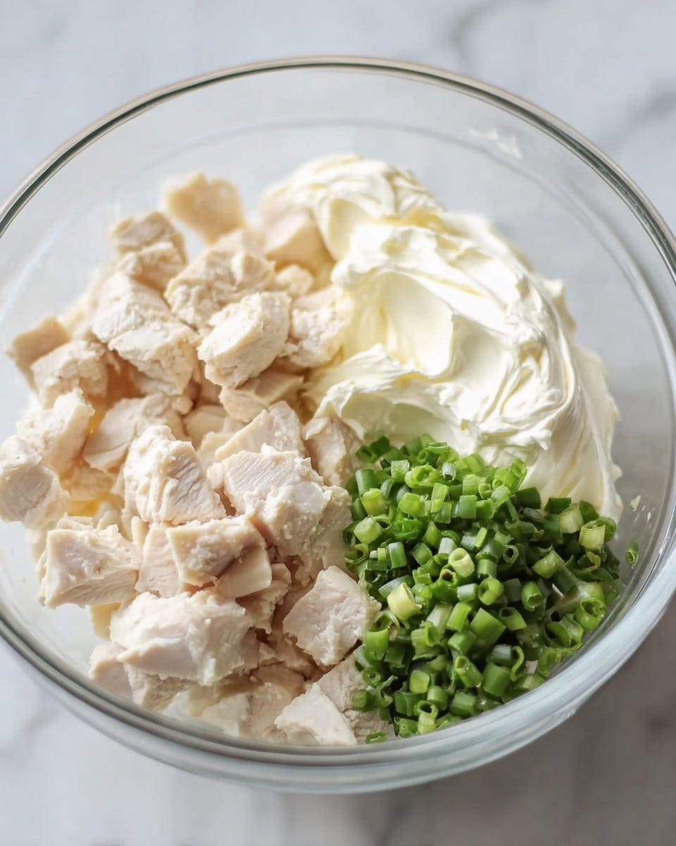 The image shows a clear glass bowl on a white marbled surface containing three layers of ingredients arranged side by side: on the left, there are chunks of light beige cooked chicken pieces with a textured, firm look; in the middle, there is a thick layer of creamy white mayonnaise with a smooth and fluffy texture; and on the right, a small pile of finely chopped bright green onions with a fresh, crisp appearance. Photo taken with an iphone --ar 4:5 --v 7