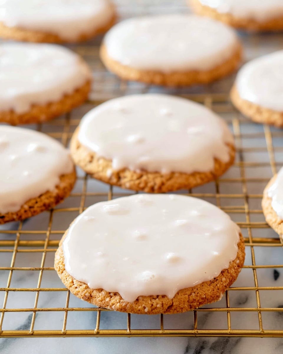 The image shows several round cookies on a metal cooling rack with a golden tone, placed on a white marbled surface. Each cookie has one layer, a rich golden-brown base with a rough texture and visible cracks, topped with a smooth, thick, white icing layer that covers the entire top surface and slightly drips over the edges. The cookies vary in size, and some icing surfaces show small bubbles or uneven spots, highlighting their homemade feel. photo taken with an iphone --ar 4:5 --v 7