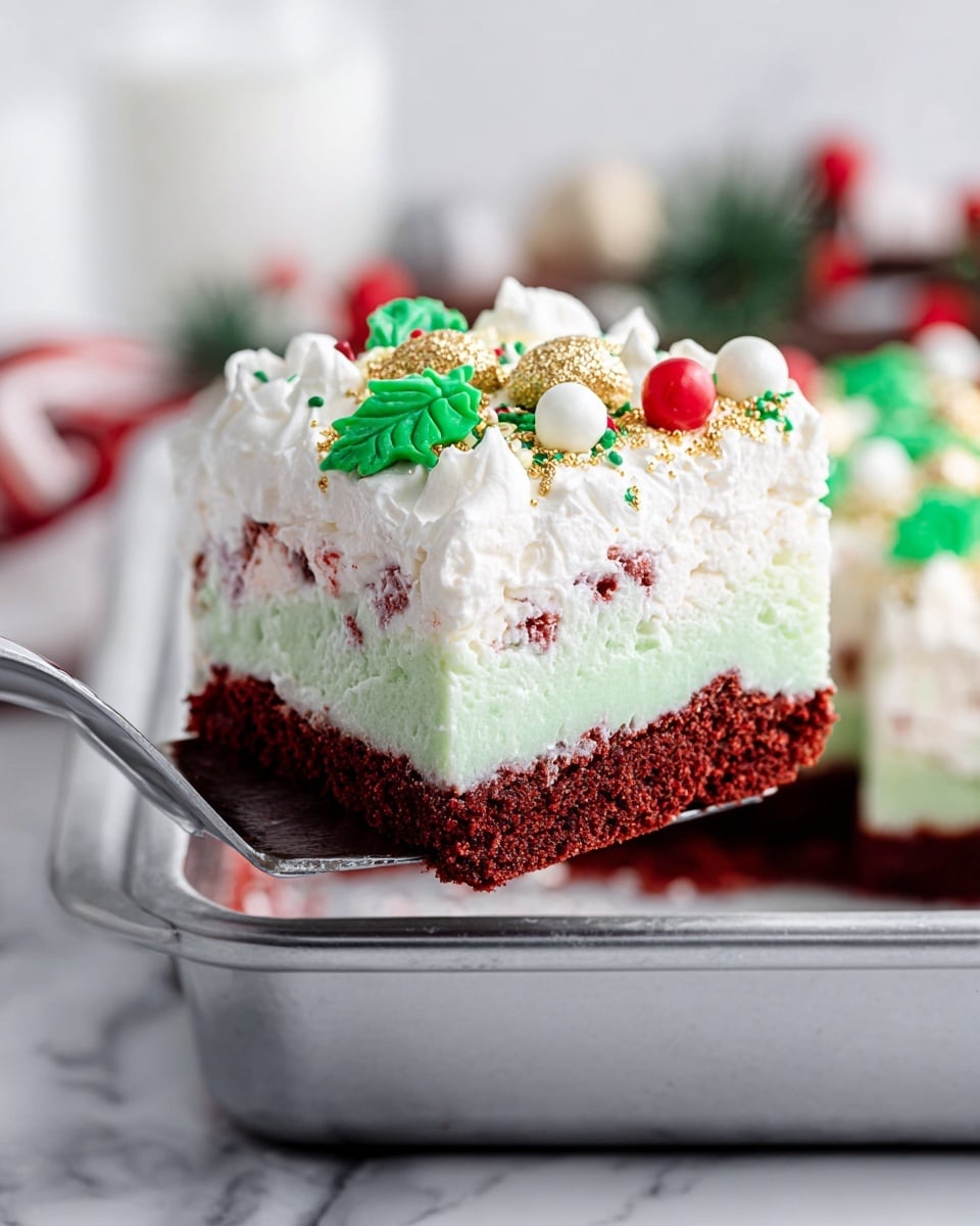 A slice of a layered dessert is shown on a metal spatula above a silver baking pan. The bottom layer is a thick, dark red cake with a moist texture. Above that is a thick white creamy layer with tiny red specks inside. The next layer is a thinner, smooth light green gel-like layer. The top layer is white fluffy whipped topping with green and white sprinkles, small gold stars, white round pearls, and a few decorative candy shapes including a red ball and a green leaf. The background has a white marbled texture and blurred holiday decorations. photo taken with an iphone --ar 4:5 --v 7