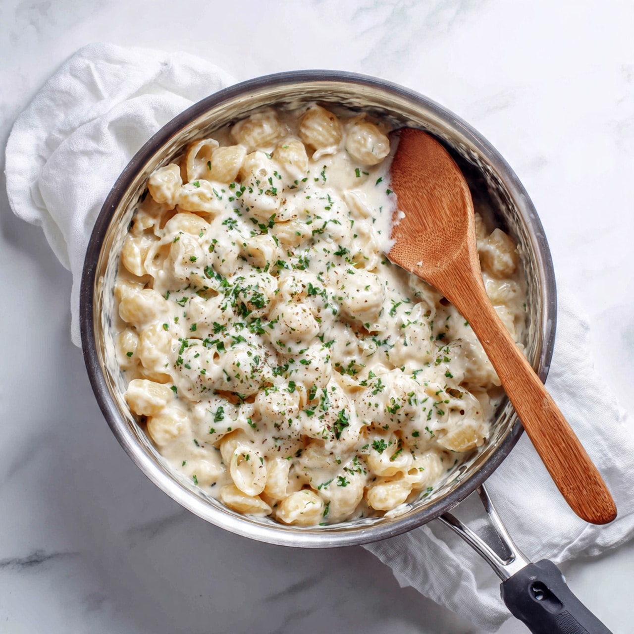 A white bowl filled with creamy tortellini pasta covered in a pale yellow cheese sauce with small green spinach pieces mixed in. The pasta is topped with fresh chopped green parsley and a light sprinkling of shredded white cheese. The bowl is set on a white marbled surface, with part of a metallic fork visible beside it. The overall look is smooth and rich with color contrast between pale sauce, light pasta, and green accents. Photo taken with an iphone --ar 4:5 --v 7
