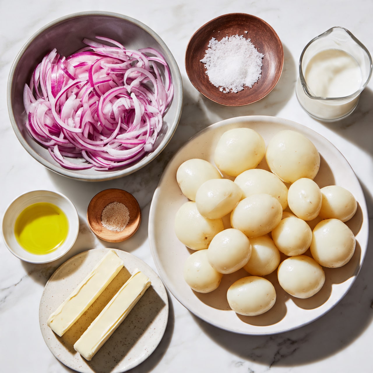 The image shows several bowls and a plate on a white marbled surface, each holding different ingredients. The largest white plate on the right is full of peeled whole potatoes, light cream in color and smooth in texture. Above it, a gray bowl contains thinly sliced red onions, pale purple and white with a soft, slightly translucent look. Below and to the left, a small white cup holds light yellow oil with a clear, smooth surface. Next to it, a small wooden plate contains a small pile of fine light brown powder. Further left, a round white plate with speckles holds three thick sticks of pale yellow butter with smooth, firm textures. Above that, a small gray bowl is filled with fine white salt. Lastly, a clear glass measuring cup holds white milk, its smooth surface shining softly. The setup is neat and evenly spaced on a white marbled texture background photo taken with an iphone --ar 4:5 --v 7