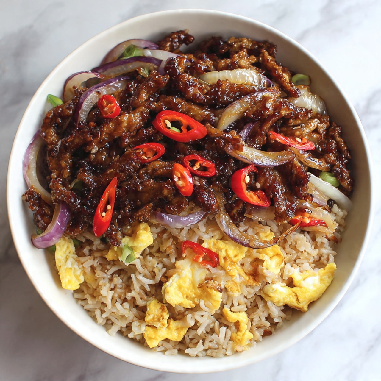 The image shows a bowl with two main layers. The bottom layer is light brown fried rice with small pieces of yellow scrambled eggs mixed in, making it look textured and fluffy. On top, there is a thick layer of dark brown cooked strips of meat covered in a shiny, sticky sauce. Mixed into the meat are thin, cooked slices of white onions and small pieces of red chili peppers, adding contrast. The bowl is white, and it sits on a white marbled surface. The photo was taken with an iphone --ar 4:5 --v 7