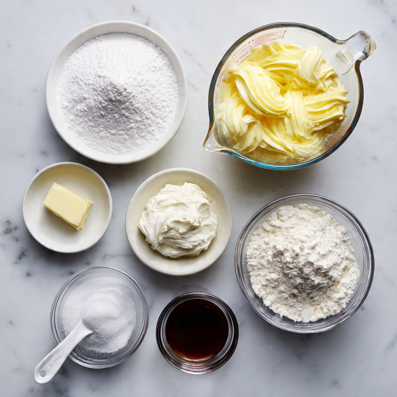 The image shows eight small bowls and a measuring spoon arranged on a white marbled surface holding different baking ingredients. At the top right is a clear glass measuring cup filled with pale yellow egg whites. To its left is a white bowl filled with fine white powdered sugar. Below the powdered sugar is a small clear bowl with white cream of tartar. To the right of that are two bowls: a larger clear glass bowl filled with white granulated sugar, and a small white measuring spoon holding white salt. Below these is a white bowl filled with white cake flour. To the right of the flour is a small clear bowl with dark brown vanilla extract, and below it is another small clear bowl with clear almond extract. The overall look is neat and bright, with the ingredients clearly labeled. photo taken with an iphone --ar 4:5 --v 7