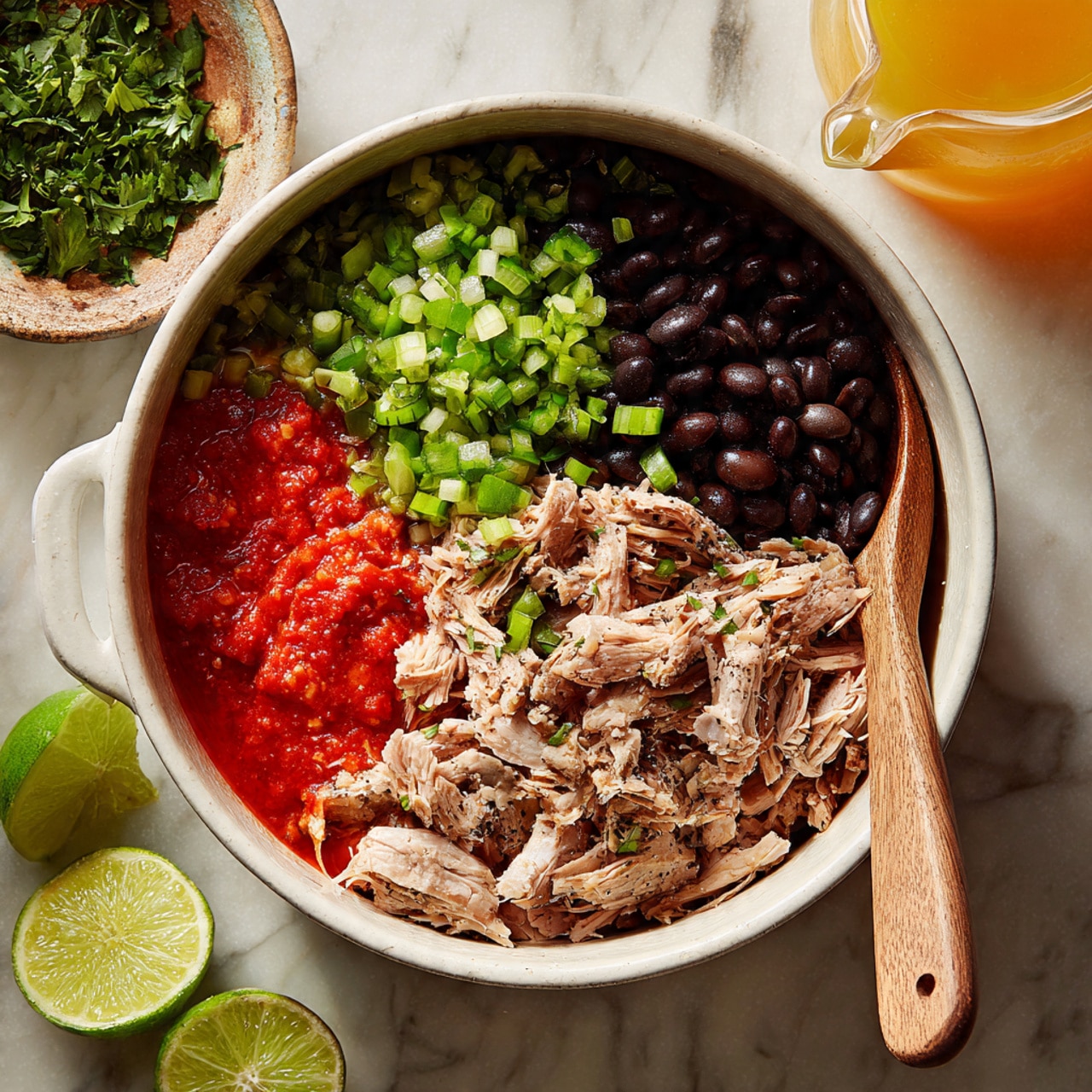 A white pot sits on a white marbled surface, filled with several layers. In the pot, at the bottom, there is a bright red chunky sauce spread on one side. On top of the sauce and beside it, there are small bright green chopped peppers piled in the middle. On another side, there are shiny black beans arranged neatly. Above these layers, there are several pieces of cooked light brown meat spread across, showing some char marks. A wooden spoon rests inside the pot on the right side. Around the pot, there is a bowl filled with green chopped herbs at the top left, two lime halves at the top right, and a glass container pouring light orange liquid into the pot from the bottom left. The whole scene is lit softly. photo taken with an iphone --ar 4:5 --v 7
