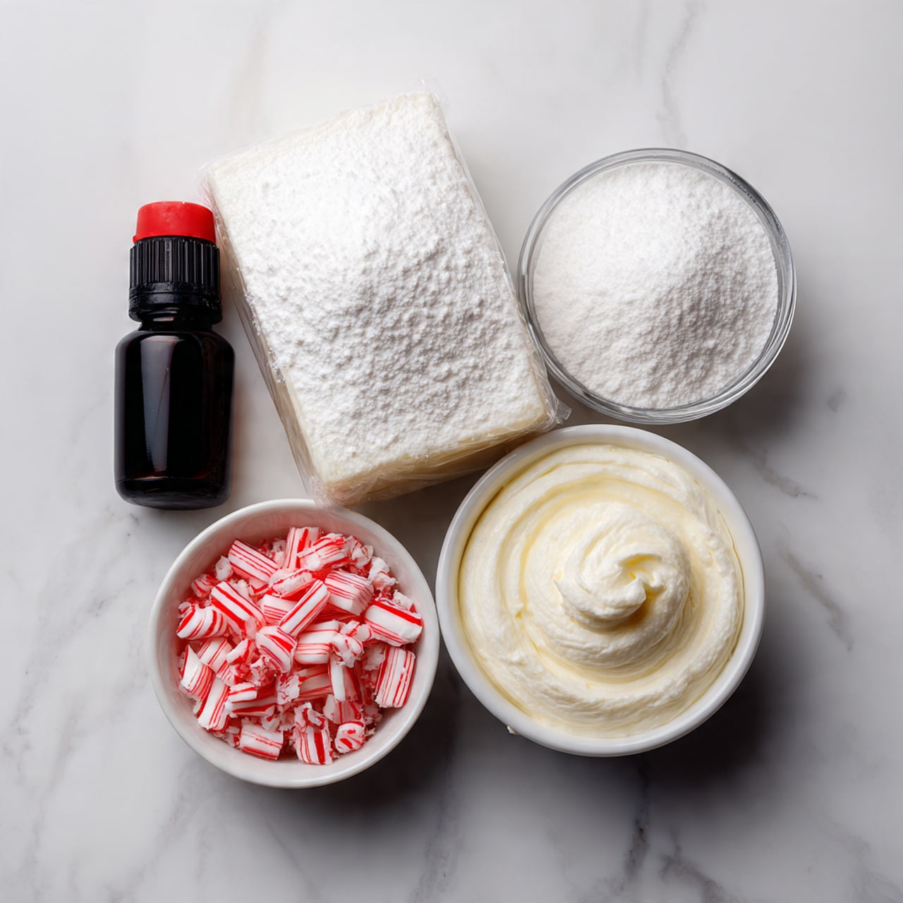 The image shows four ingredients on a white marbled surface: a clear glass bowl with white powdered sugar, a clear glass bowl filled with chopped red and white peppermint candy, a silver wrapped block of cream cheese, a white bowl with smooth, creamy white frosting, and a small black bottle with a red cap, likely vanilla extract. The items are arranged in a loose square shape with the frosting bowl at the bottom center, the powdered sugar at the top left, the peppermint candy at the top right, the cream cheese block at the left center, and the vanilla bottle at the right center photo taken with an iphone --ar 4:5 --v 7