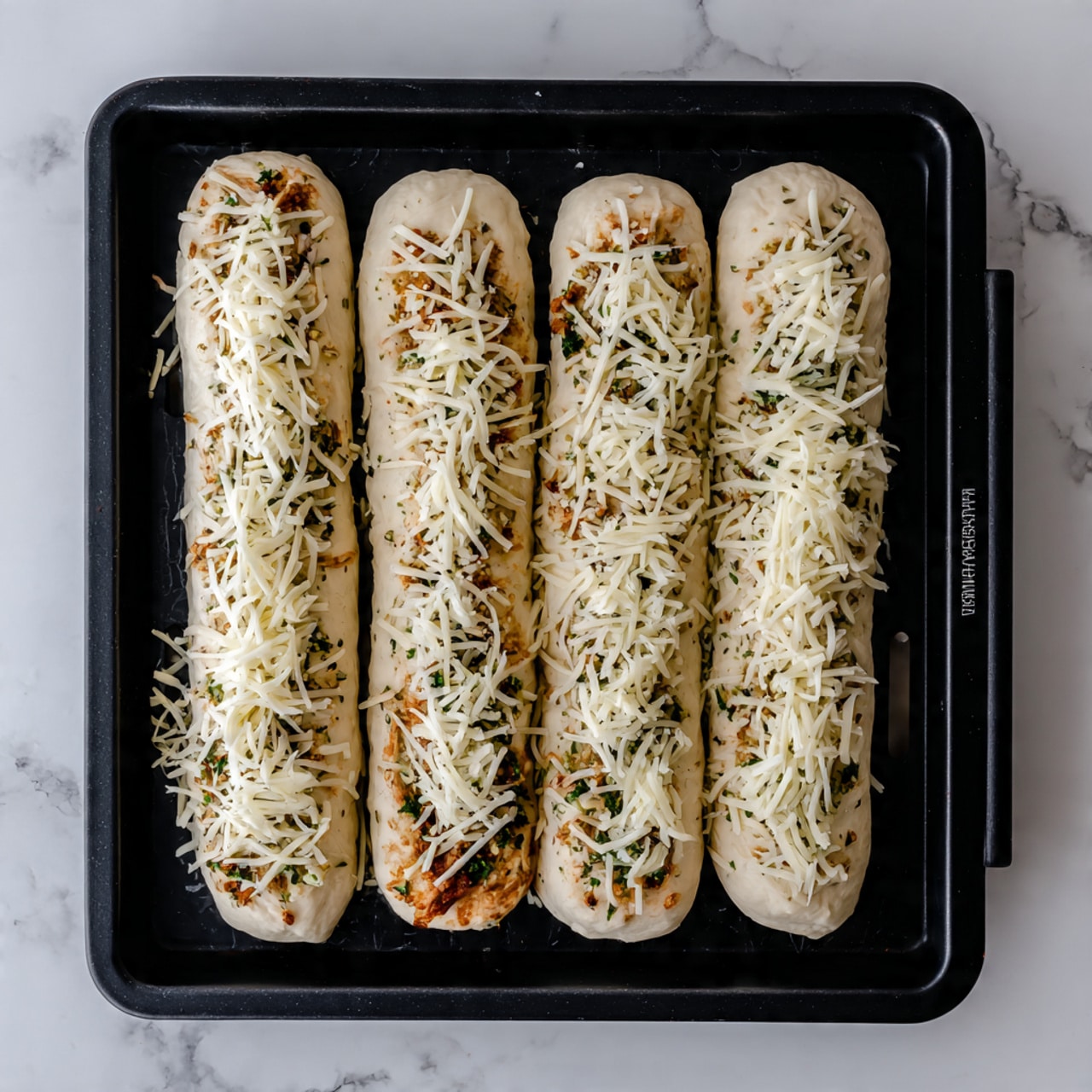 The image shows four long dough sticks placed in a black baking tray with individual slots for each stick. Each dough stick is white and topped with a mix of finely grated cheese and herbs, giving a speckled light brown and greenish texture across the surface. The dough sticks are arranged side by side in the tray, which rests on a white marbled surface. The overall look is neat and ready for baking. photo taken with an iphone --ar 4:5 --v 7