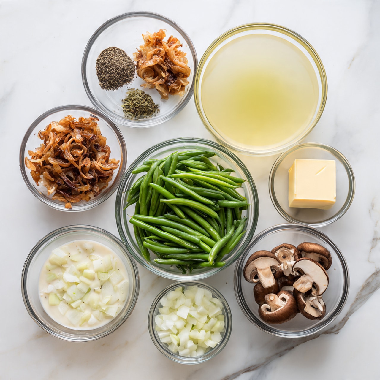 The image shows eight clear glass bowls arranged on a white marbled surface, each filled with different ingredients. In the center is a bowl of bright green cut green beans. Above it to the right is a large bowl filled with pale yellow chicken broth, and above that is a smaller bowl with a square piece of light yellow butter. To the left of the green beans is a bowl filled with crispy browned fried onions, and above that is a small bowl of mixed black salt and pepper. Below the green beans is a bowl of creamy white soup with bits of mushroom visible, and to the right of that is a bowl of sliced brown mushrooms. To the right of the green beans but slightly above is a small bowl with diced white onions. Each bowl is clear and allows a view of the color and texture of the ingredient inside, all resting on the white marbled surface. Photo taken with an iphone --ar 4:5 --v 7