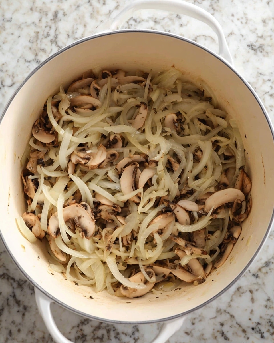 The image shows a white pot filled with a mix of cooked thinly sliced onions and chopped mushrooms. The onions are pale white and slightly translucent, curling gently in long thin strips spread across the top. The mushrooms are light brown with darker edges, scattered evenly throughout the onions, creating a textured blend of light beige and soft brown tones. The pot rests on a white marbled surface, and the overall look is a soft mixture of curved and irregular shapes with a moist texture. Photo taken with an iphone --ar 4:5 --v 7