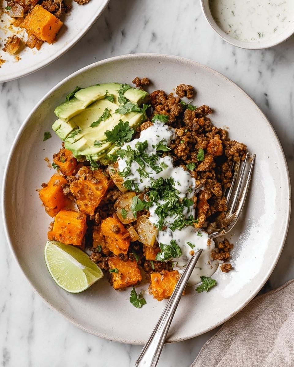 A white plate sits on a white marbled surface, filled with a layered dish. The bottom layer has roasted orange chunks, likely squash, with a soft texture. On top, there is browned ground meat mixed with small pieces of cooked onion. A small portion of green avocado slices rests on one side, sprinkled with chopped fresh herbs. White creamy sauce is dolloped over the meat layer, with extra sauce on the side dishes. Beside the food on the plate, a wedge of lime adds color. A white fork is placed on the right side of the plate, partly under the food. Photo taken with an iphone --ar 4:5 --v 7