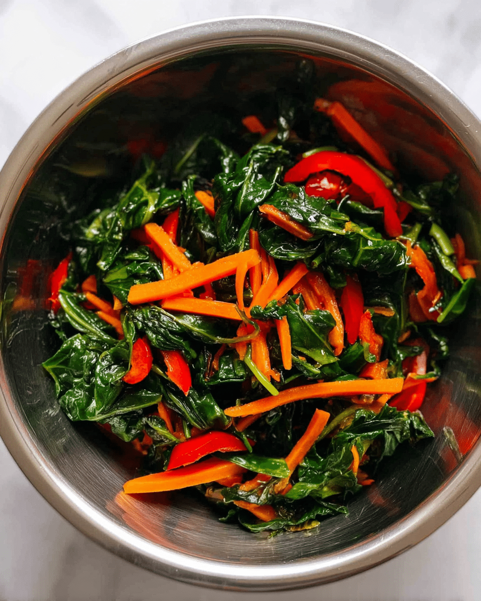 A shiny metal bowl holds a mix of cooked green leafy vegetables, thin bright orange carrot sticks, and thin red bell pepper slices, all mixed together with visible texture on the leaves and the crispness of the vegetables, set on a white marbled surface photo taken with an iphone --ar 4:5 --v 7