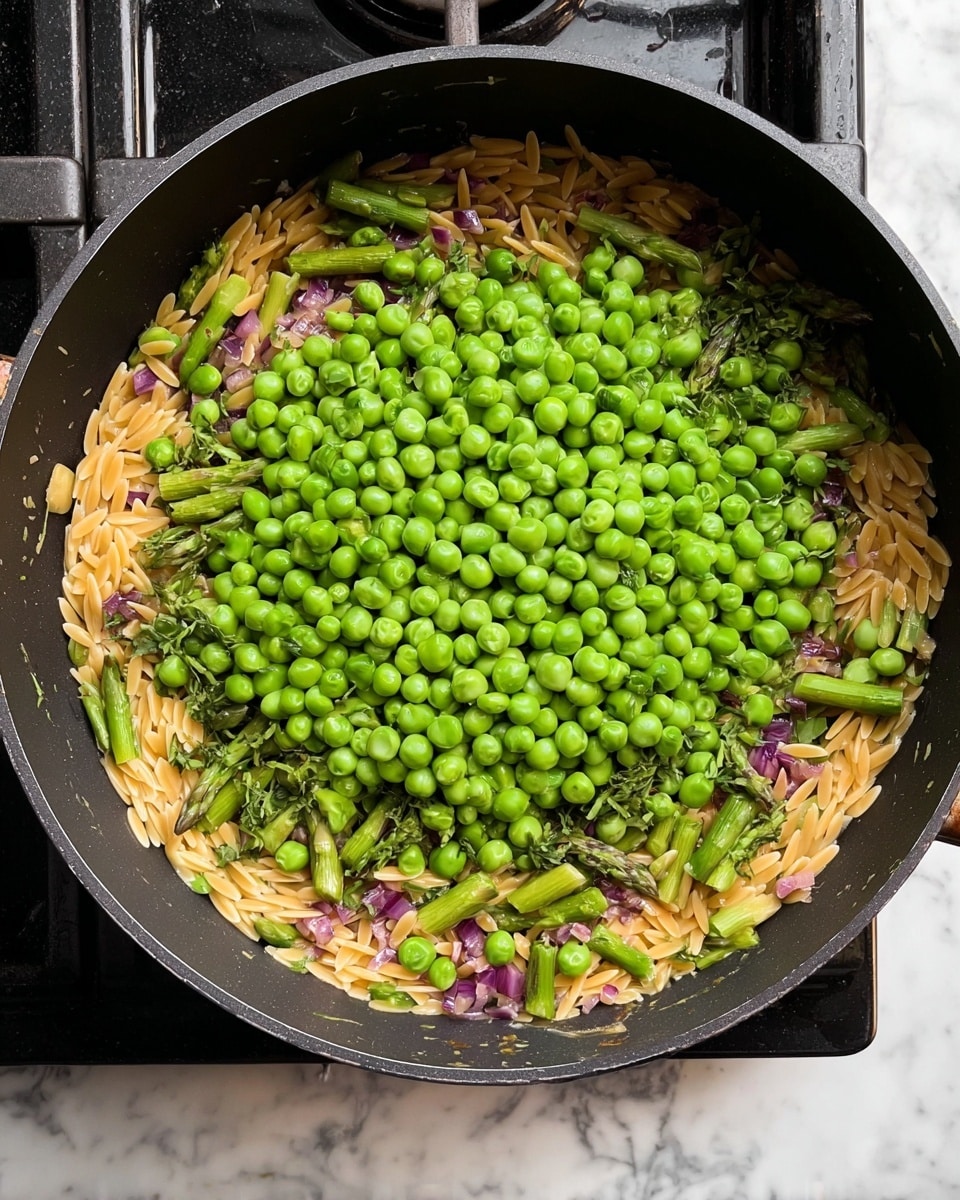 A black pan filled with three main layers: the bottom layer is light golden orzo pasta mixed with small bits of purple onions, giving texture and color contrast, the middle layer shows bright green asparagus pieces cut into small sections and scattered evenly, and on top is a pile of fresh green peas, vibrant and round, covering the center part of the pan. The pan is sitting on a black stovetop with white marbled background visible around it. photo taken with an iphone --ar 4:5 --v 7