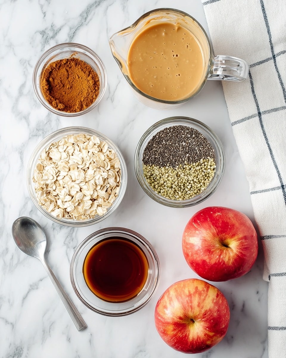 The image shows ingredients for a recipe arranged on a white marbled surface. There are two bright red apples with a smooth skin placed side by side at the bottom right. Above them, a small clear glass bowl holds a layer of brown cinnamon powder. Next to it, a larger clear glass bowl is filled with half black chia seeds and half light green hemp seeds, side by side. On the left, there is a metal spoon filled with light beige rolled oats, and below it, a small clear glass bowl with dark brown vanilla extract. Above these, there is a medium clear glass bowl with light brown creamy peanut butter with a smooth texture and a larger clear glass measuring cup filled with a light beige liquid, likely almond milk. A white towel with blue checks is visible in the top right corner. Photo taken with an iphone --ar 4:5 --v 7