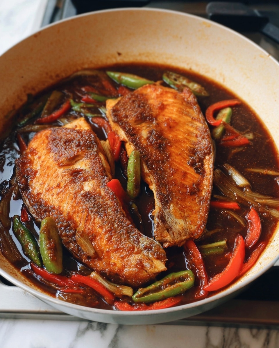 The image shows two large pieces of orange-brown cooked fish with a slightly crispy texture on the outside, lying in a white pan. Around the fish, there are thin slices of red bell pepper and some green chili peppers, all mixed in a dark brown sauce. The sauce looks thick and glossy, covering the bottom of the pan, and giving the dish a rich look. The fish is the main focus, with the peppers and sauce adding color contrast around it. The pan is placed on a cooktop with a white marbled surface in the background. photo taken with an iphone --ar 4:5 --v 7