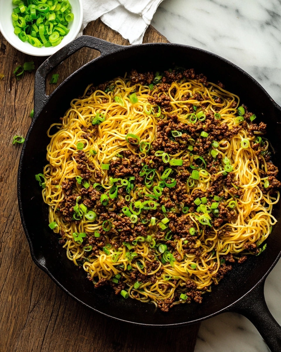 A black cast iron pan filled with thin yellow noodles mixed with small dark brown cooked minced meat and scattered green onion slices on top; the noodles and meat fill the pan evenly and some green onions are sprinkled across the surface. The pan handle extends to the right side. In the top left corner, a small white bowl holds chopped green onions, and the setting is on a white marbled surface. photo taken with an iphone --ar 4:5 --v 7