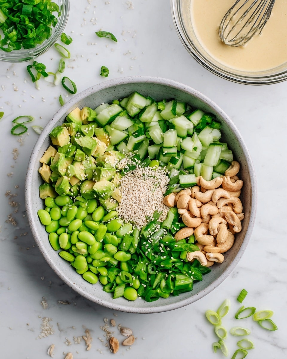 A bowl filled with five main layers: bright green chopped cucumbers on the top right, sliced green onions on the top left, diced light green avocado on the bottom left, vibrant green edamame beans on the bottom right, and a small pile of beige cashew nuts with white sesame seeds in the center. The bowl is round and white, placed on a white marbled surface with scattered sesame seeds and pieces of green onion around it. In the upper right corner, there is a glass bowl containing a creamy light beige sauce with a small whisk inside. The image is bright, fresh, and clean. photo taken with an iphone --ar 4:5 --v 7