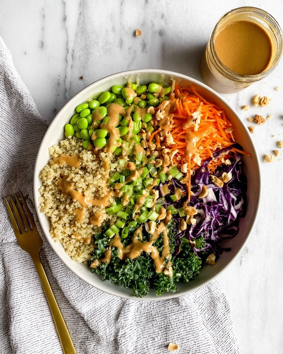 A white bowl filled with six different sections of food: light beige quinoa on the top left with a drizzle of creamy light brown sauce, bright green edamame beans with chopped nuts on the top middle, finely shredded orange carrots with sauce and nuts on the top right, dark purple shredded cabbage with a drizzle of sauce on the bottom left, light green chopped scallions with some sauce and nuts in the bottom middle, and dark green curly kale with sauce and nuts on the bottom right. Next to the bowl is a small glass jar of light brown creamy sauce, scattered nut pieces, and a gold fork resting on a white and gray striped cloth on a white marbled surface. photo taken with an iphone --ar 4:5 --v 7