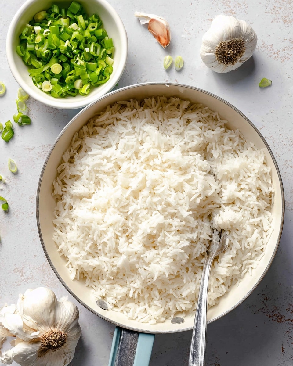 A white pan filled with fluffy cooked white rice showing separate grains with a slightly shiny texture, a metal fork resting inside the pan on the right side. Next to the pan, there is a small white bowl filled with chopped bright green spring onions, and near the bowl, there are a few garlic cloves and bulbs placed on a white marbled surface. The colors are soft and natural with a light background that highlights the freshness of the ingredients. photo taken with an iphone --ar 4:5 --v 7