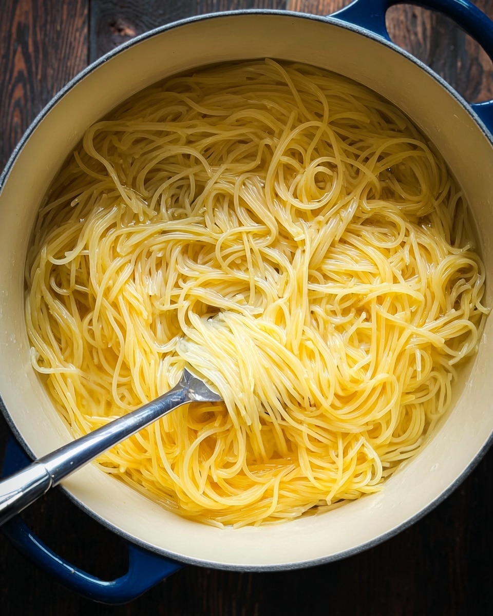 A pot filled with light yellow cooked spaghetti noodles submerged in clear water. The thin strands of spaghetti are soft and tangled, with a silver pasta server spoon in the center lifting some noodles. The inside of the pot is cream colored, and the pot’s outer edge is dark blue. The pot is placed on a dark wooden surface. Photo taken with an iphone --ar 4:5 --v 7