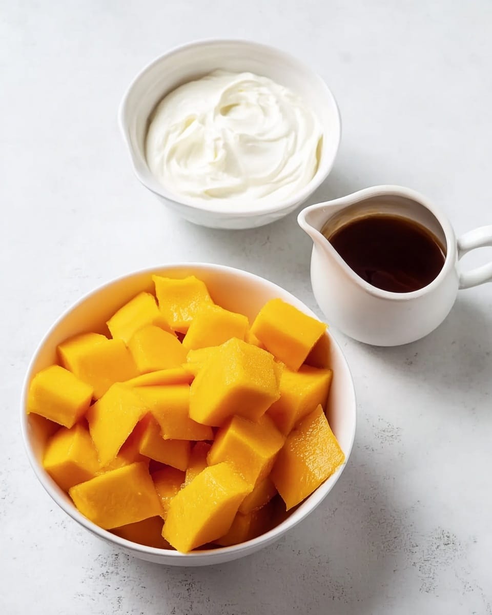 A white bowl filled with bright orange chopped mango pieces that look soft and juicy, the large chunks layered unevenly in the bowl. Next to it on the white marbled surface is a white bowl with smooth creamy white yogurt, swirled lightly inside, and a small white pitcher with dark brown syrup that has a shiny surface. The scene shows a clean, fresh arrangement with a top-down view. photo taken with an iphone --ar 4:5 --v 7