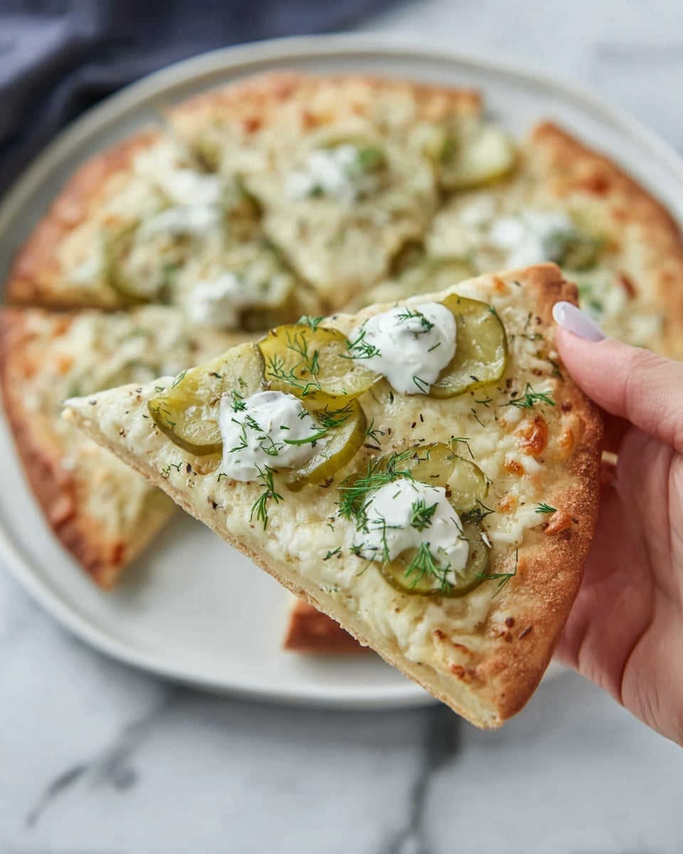 A close-up image of a pizza slice held by a woman's hand. The pizza has a golden-brown crust with a slightly thick edge. The first layer is melted white cheese, covering the whole slice evenly, followed by thin green pickle slices spread on top. Small dollops of white creamy sauce are scattered across the slice, with finely chopped green herbs sprinkled all over. In the background, there is a whole pizza with the same toppings on a white plate, placed on a white marbled surface. photo taken with an iphone --ar 4:5 --v 7
