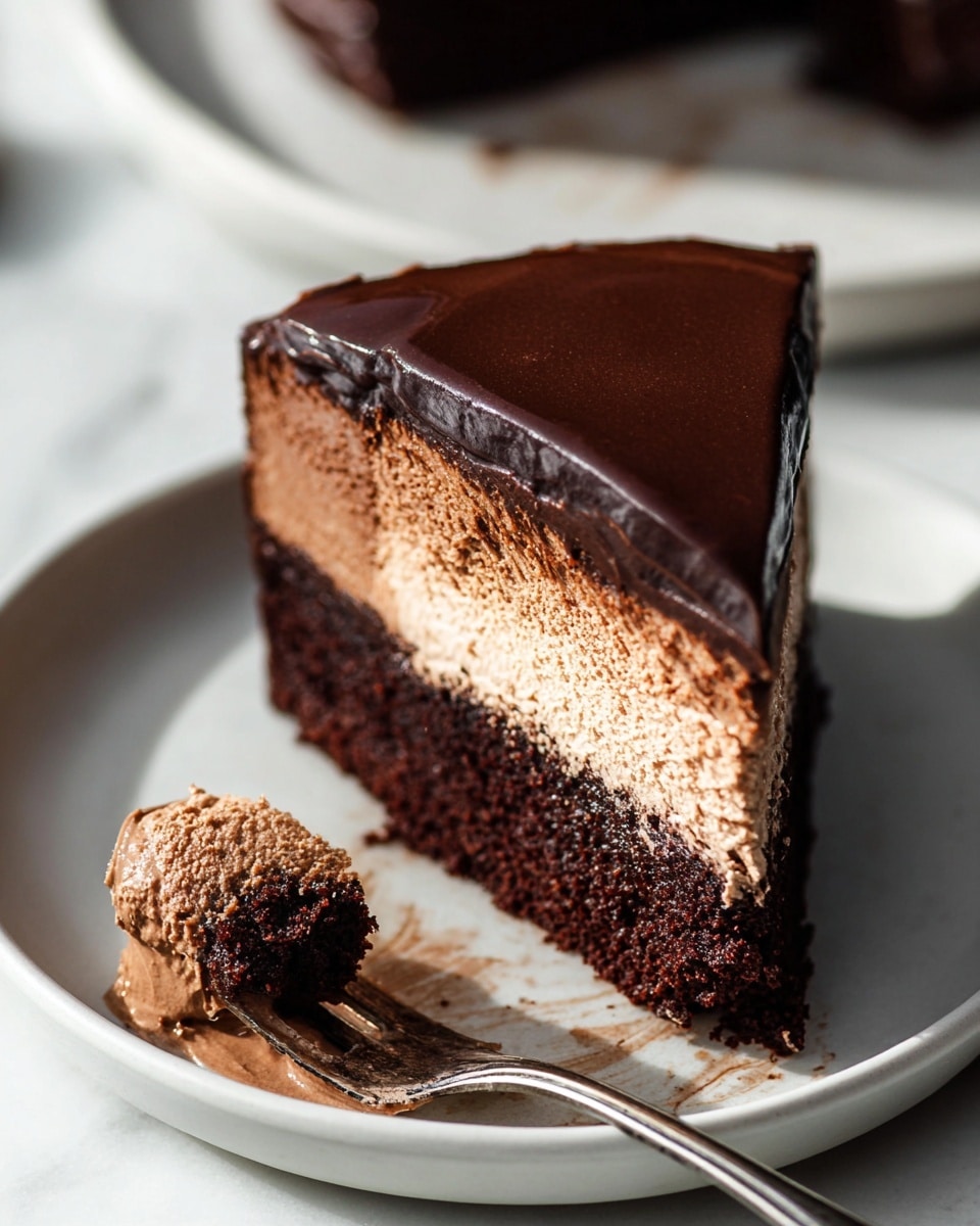 A slice of chocolate cake featuring two thick layers is placed on a white plate on a white marbled surface. The bottom layer is dark brown and dense with a moist texture, while the middle layer is a thick, light brown chocolate mousse with a creamy and smooth texture. The top and sides of the slice are covered with a glossy, dark chocolate ganache that has a slightly rippled surface. Next to the cake, a fork holds a small bite-sized piece covered in light brown mousse. There are smudges of ganache and mousse on the plate, adding a sense of richness and indulgence. The photo taken with an iphone --ar 4:5 --v 7