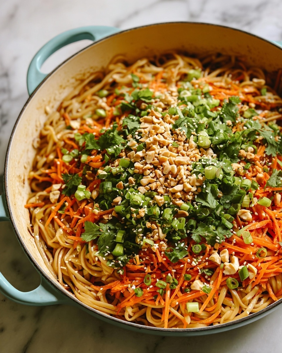 The dish shown is a pan with cooked noodles at the bottom, light brown and slightly glossy, forming the first layer. On top of the noodles, finely chopped green onions and fresh cilantro leaves create a fresh green layer. Above that, shredded bright orange carrots add a colorful and textured layer, scattered with light brown chopped peanuts and white sesame seeds, giving a crunchy appearance. The pan is white, and the background surface has a white marbled texture. photo taken with an iphone --ar 4:5 --v 7