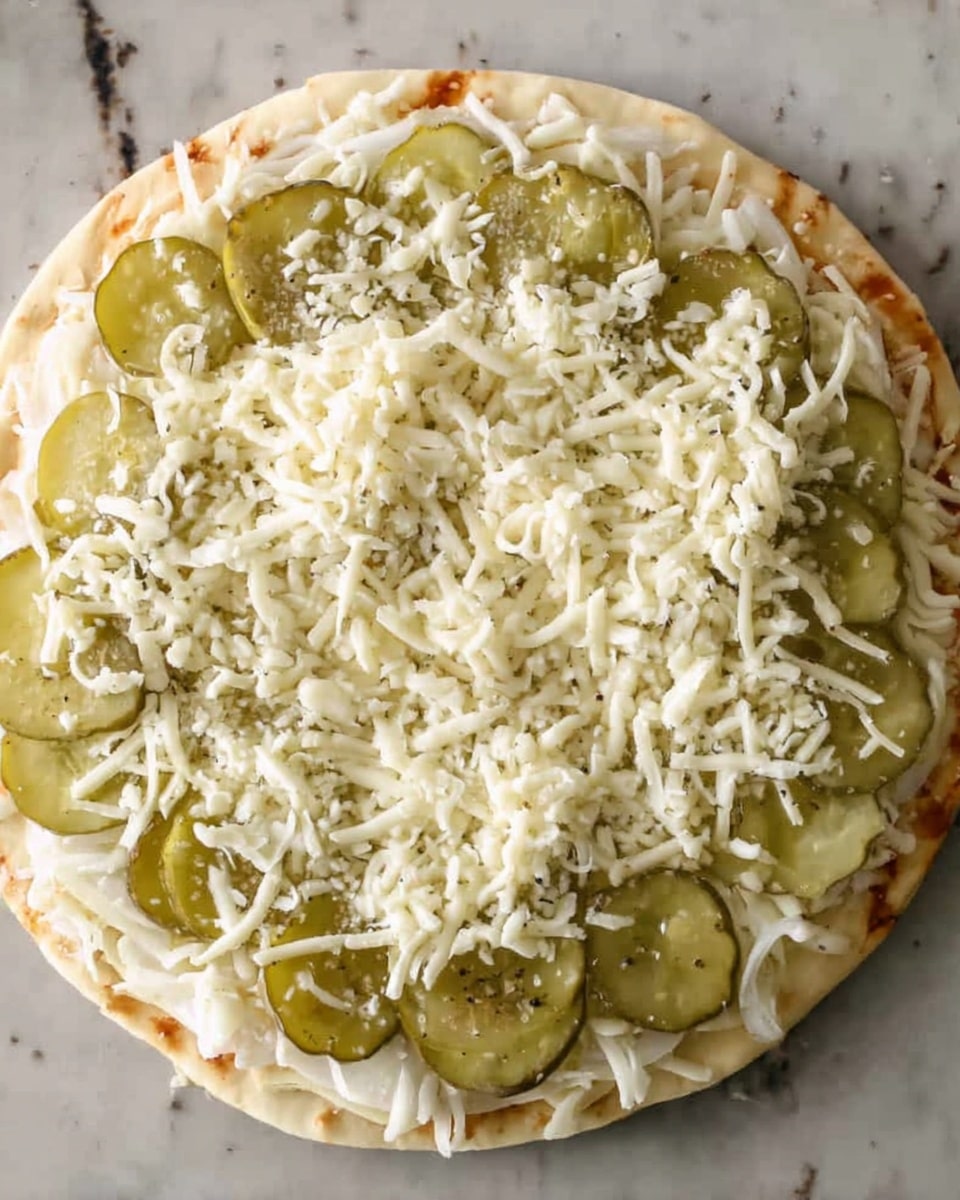 A round flat pizza crust forms the base of the dish, topped with a first layer of evenly spread, light green pickle slices arranged across the surface. On top of the pickles is a layer of thin white sliced onions scattered across, partly covering the pickles. The final layer consists of shredded white cheese generously spread over the onions and pickles, adding texture and thickness. The pizza is set on a white marbled surface. Photo taken with an iphone --ar 4:5 --v 7