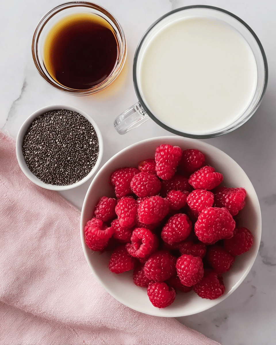 The image shows a white bowl filled with bright red raspberries at the bottom right. Above the bowl to the left, there is a small white bowl with tiny black chia seeds with a bumpy texture. To the top left, there is a clear small glass bowl filled with dark brown liquid, likely syrup. To the top right, there is a clear glass mug filled with white milk. The items are placed on a light pink cloth on top of a white marbled surface. photo taken with an iphone --ar 4:5 --v 7