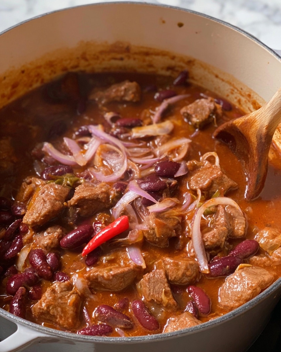 The image shows a close-up of a white pot filled with a thick stew featuring multiple layers of ingredients. The stew has tender chunks of brown meat scattered throughout a rich, reddish-brown sauce that looks savory and slightly oily. There are dark red kidney beans mixed in, adding texture and a deep burgundy color. Thin slices of light purple onions are visible layered within the stew, along with a whole red chili pepper adding a bright pop of red. The stew is being stirred with a wooden spoon, which is partially visible on the right side. The background surface is a white marbled texture. photo taken with an iphone --ar 4:5 --v 7