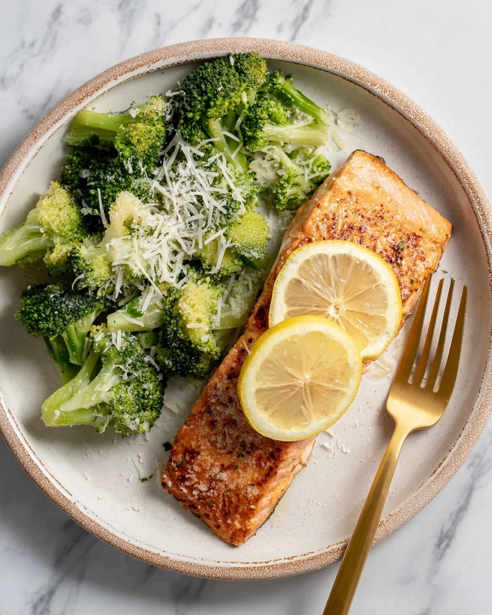 This image shows a single piece of cooked salmon fillet at the bottom right of a white ceramic plate with a rustic edge. On top of the salmon, two lemon wedges are placed side by side, showing their pale yellow color and juicy texture. Above the salmon, there is a pile of bright green broccoli florets with a few scattered grains of grated cheese on top, giving a light white contrast. A gold fork lies along the right edge of the plate, resting partly on the plate and partly outside. The plate is set on a white marbled surface. photo taken with an iphone --ar 4:5 --v 7